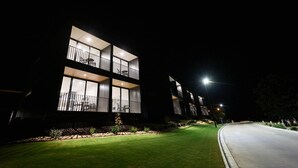 Un edificio moderno con varios balcones, ventanas amplias y un exterior iluminado por la noche.