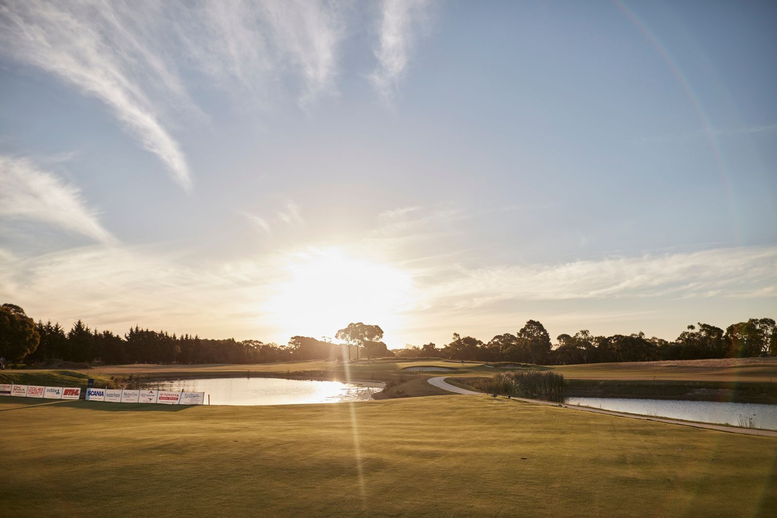 Un campo de golf con un estanque, árboles y cielo despejado.
