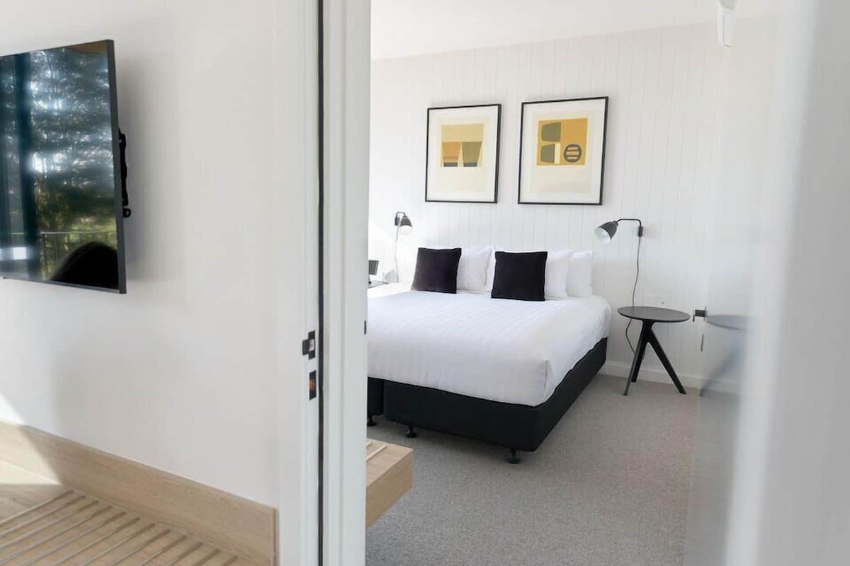Un dormitorio moderno con cama, mesitas de noche y televisor montado.