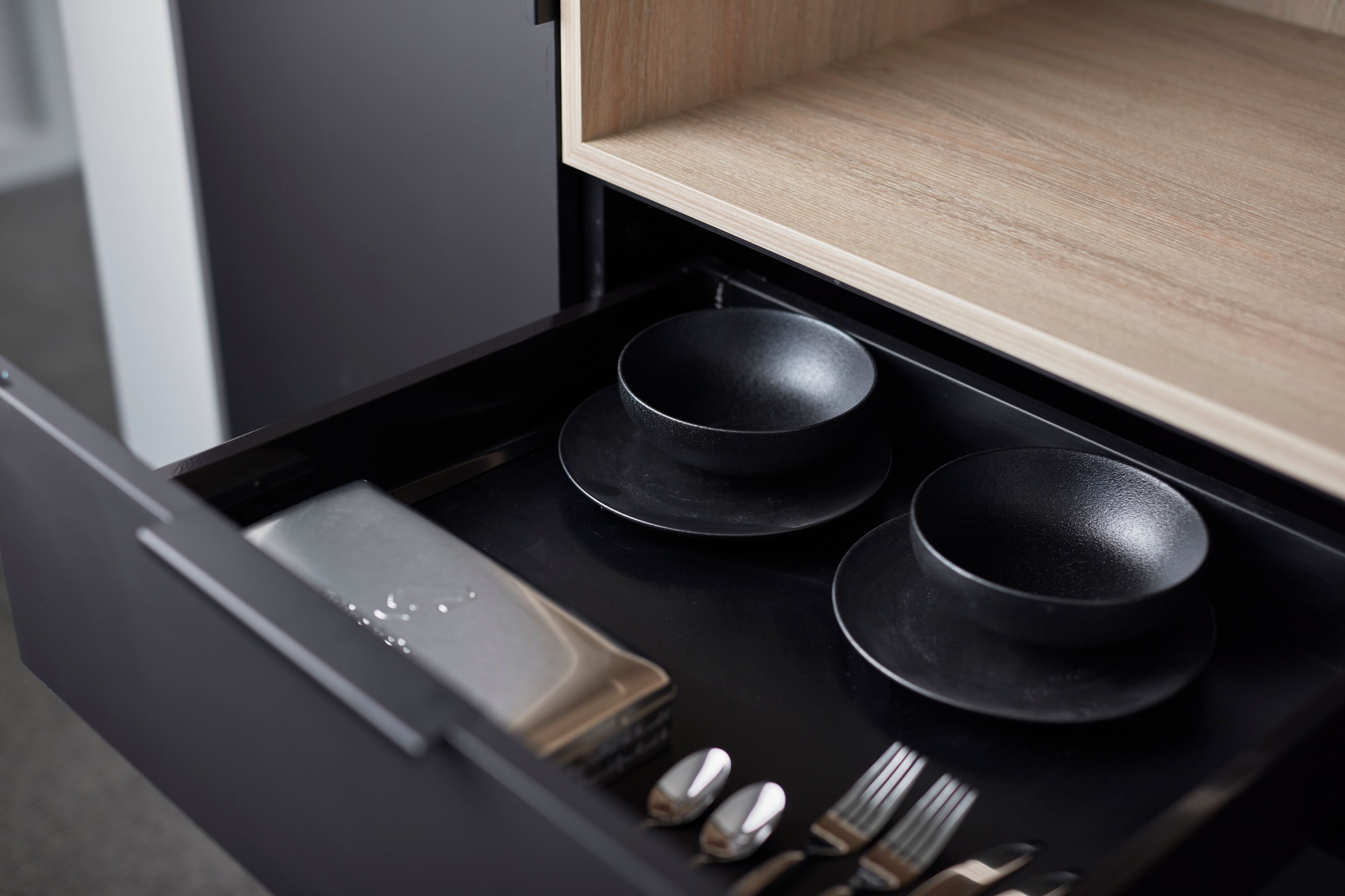 A black drawer with three black bowls, a small tray, and some utensils.