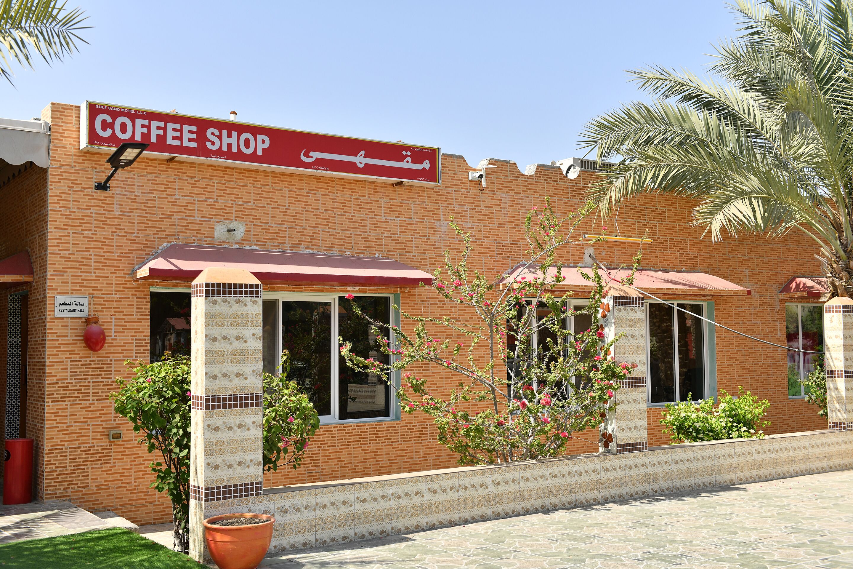 A coffee shop with a red awning, brick facade, and potted plants.