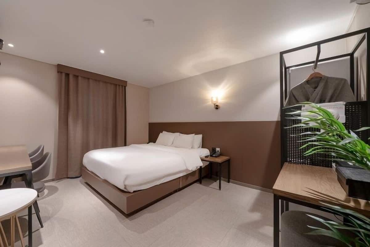 A hotel room with a bed, bedside table, chair, desk, and a mirror.