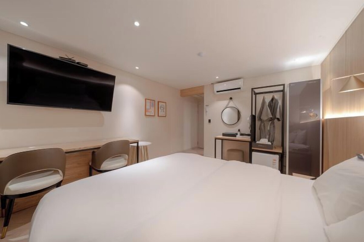 Una habitación de hotel moderna con una cama grande, un televisor de pantalla plana en la pared, un escritorio con una silla, una mesita pequeña y un armario.