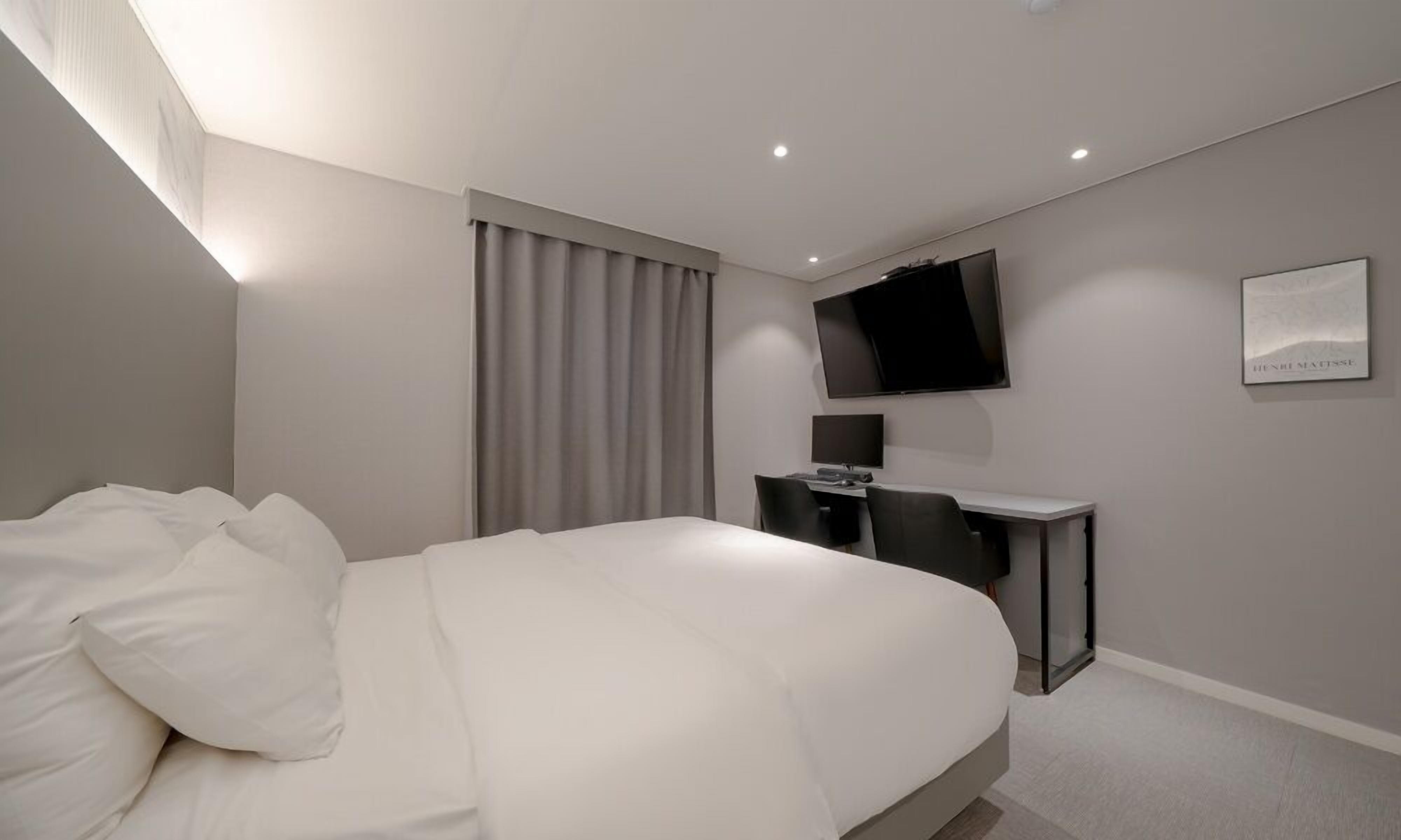 A modern hotel room with a large bed, a desk, and a flat-screen TV mounted on the wall.