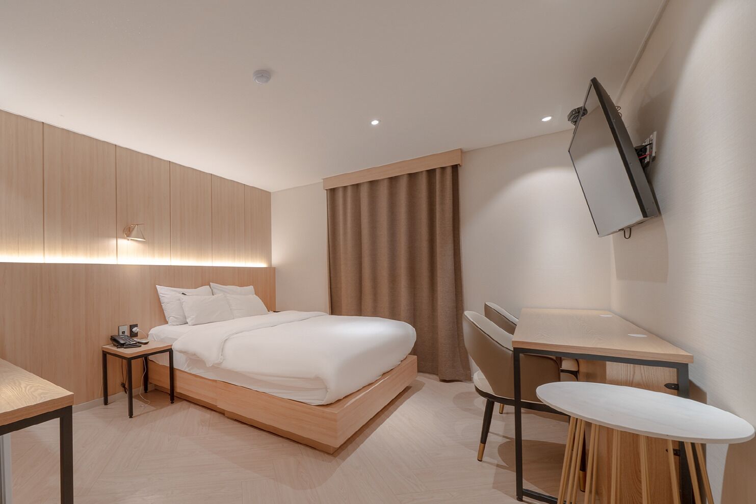 Ein modernes Hotelzimmer mit Bett, Nachttisch, Schreibtisch und einem an der Wand befestigten Flachbildfernseher.