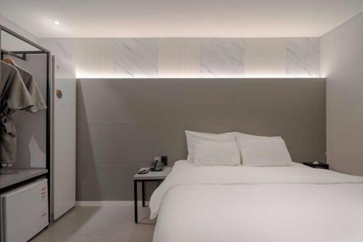Una habitación de hotel moderna con una cama grande, una mesita de noche con teléfono y un armario.