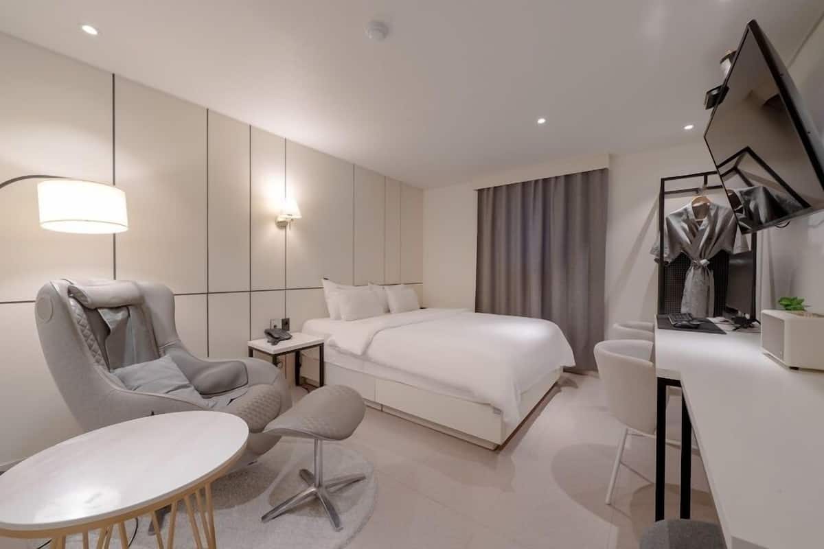 A modern hotel room with a bed, a desk, a chair, a sofa, and a TV.