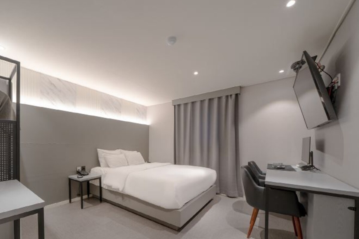 Habitación de hotel moderna con cama, escritorio, silla y televisor montado en la pared.