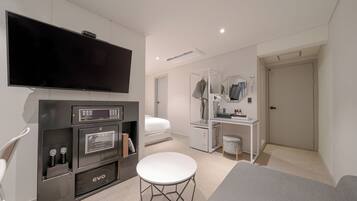 A modern hotel room with a flat-screen TV, a minibar, a desk with a mirror, a vanity, and a bed.