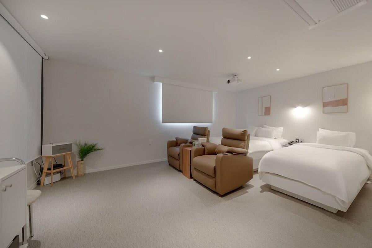A modern hotel room with a large bed, two sofas, a desk, and a small plant.