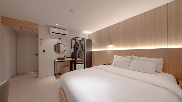 A modern hotel room with a large bed, wooden paneling on the walls, a desk with a chair, and a wardrobe.