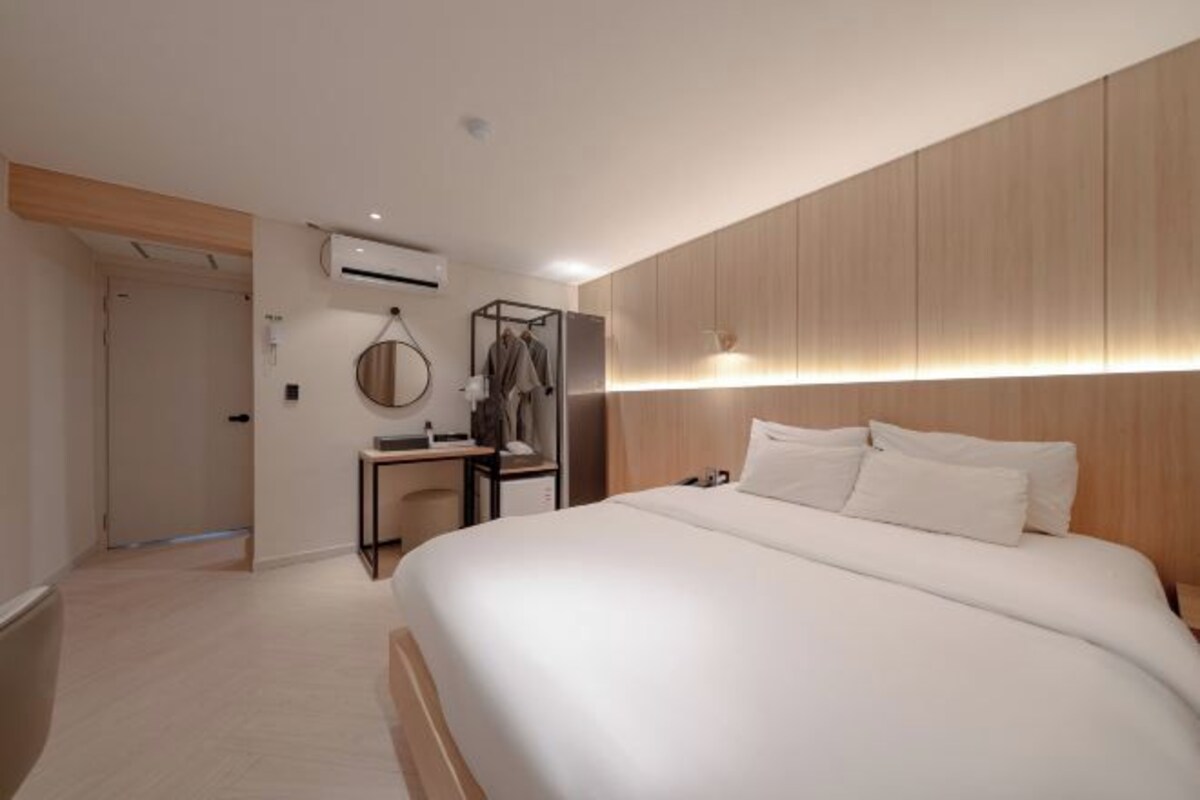 Una habitación de hotel moderna con una cama grande, una mesita de noche, un armario y un equipo de aire acondicionado instalado en la pared.