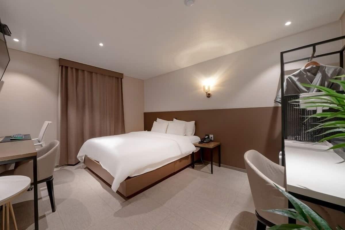 A hotel room with a bed, a desk with a chair, a TV, and a mirror.