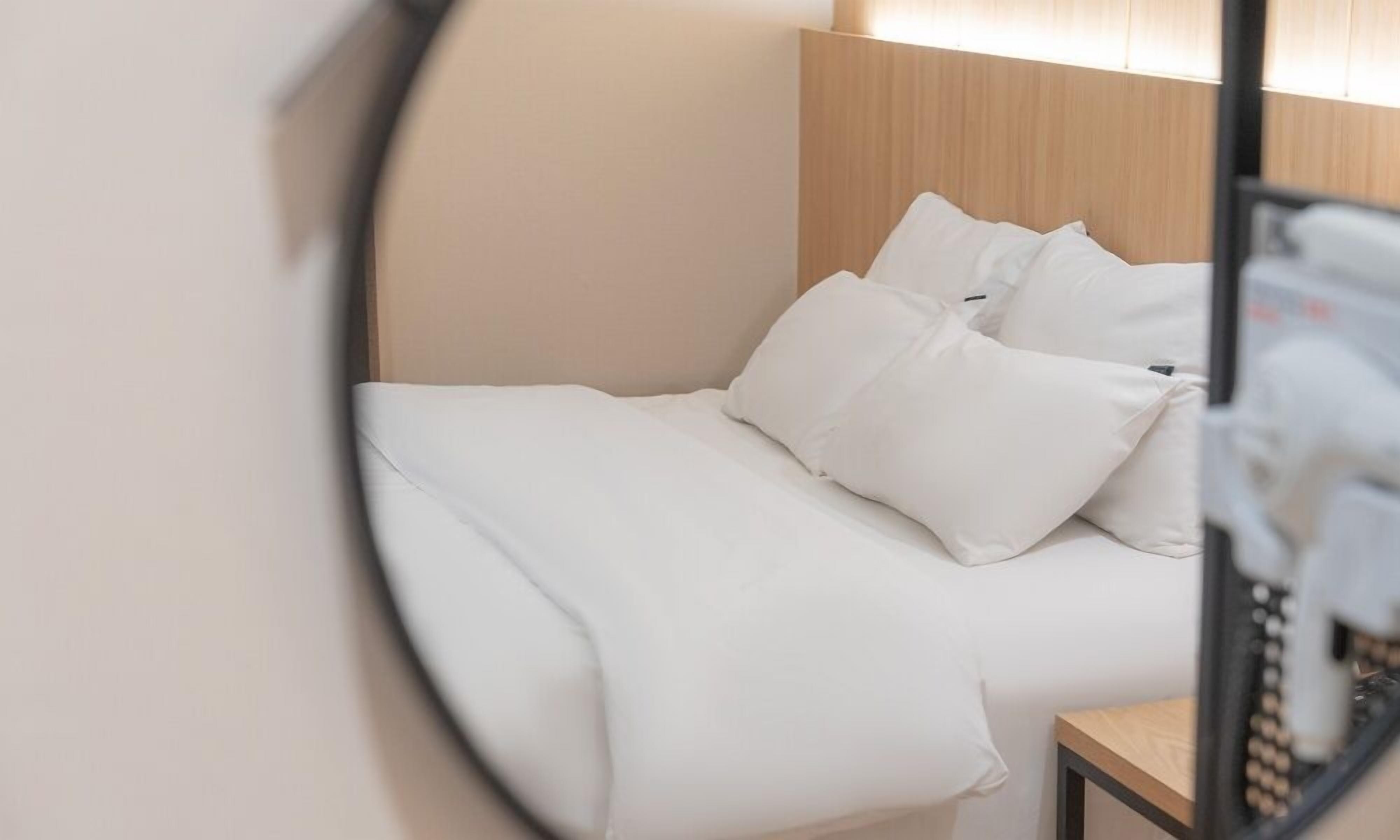 Un lit bien fait, avec du linge de lit blanc et des oreillers, une tête de lit en bois et une petite table de chevet avec une lampe.