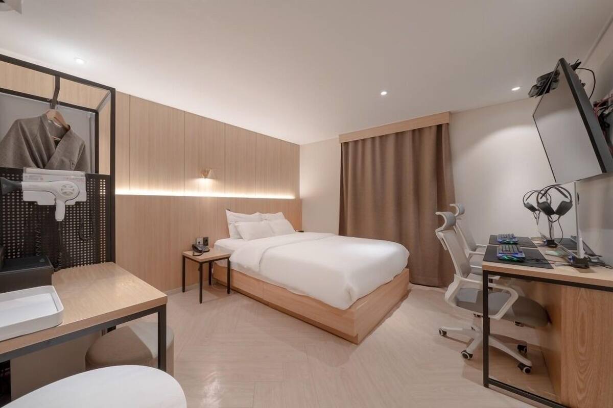 A modern hotel room with a bed, desk, chair, and a mirror.