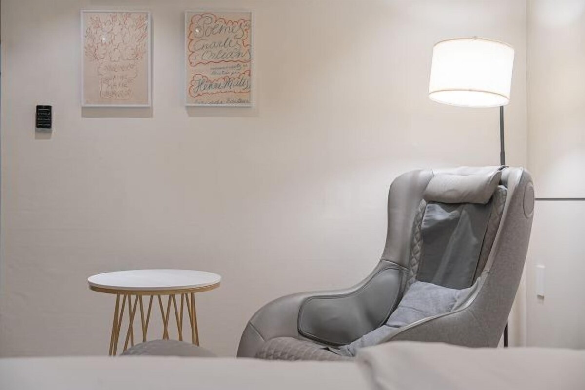 A room with a massage chair, a small round table, and two framed artworks on the wall.
