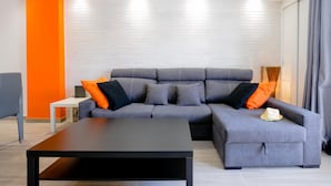 Un salon moderne avec un canapé d’angle gris, une table basse noire et un mur d’accent de couleur orange vif.