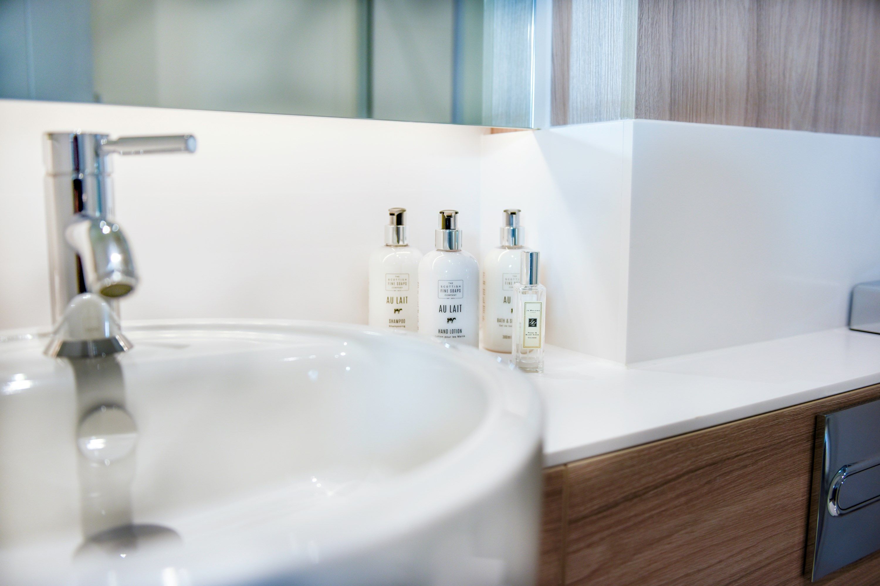 Un baño con un lavabo blanco, un espejo y tres botellas de loción para manos sobre la encimera.