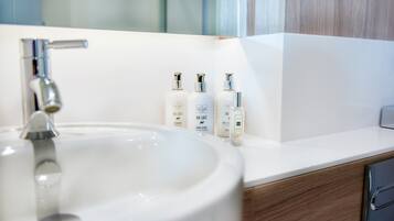 Un baño con un lavabo blanco, un espejo y tres botellas de loción para manos sobre la encimera.