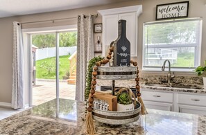 Una cucina con un espositore in legno a tre livelli che contiene una bottiglia di vino, un cartello con la scritta 'Coffee' e una pianta grassa.