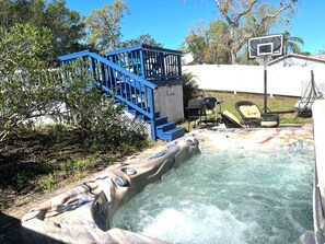 A hot tub with a wooden design, a blue staircase, and a basketball hoop in a backyard setting. - Spacious Estate Home with large Pool and Jacuzzi, Near Beaches, Springs & Tampa (Spring Hill)