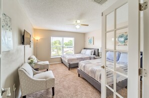 A bedroom with two beds, a chair, a desk, a ceiling fan, and artwork on the walls. - Spacious Estate Home with large Pool and Jacuzzi, Near Beaches, Springs & Tampa (Spring Hill)