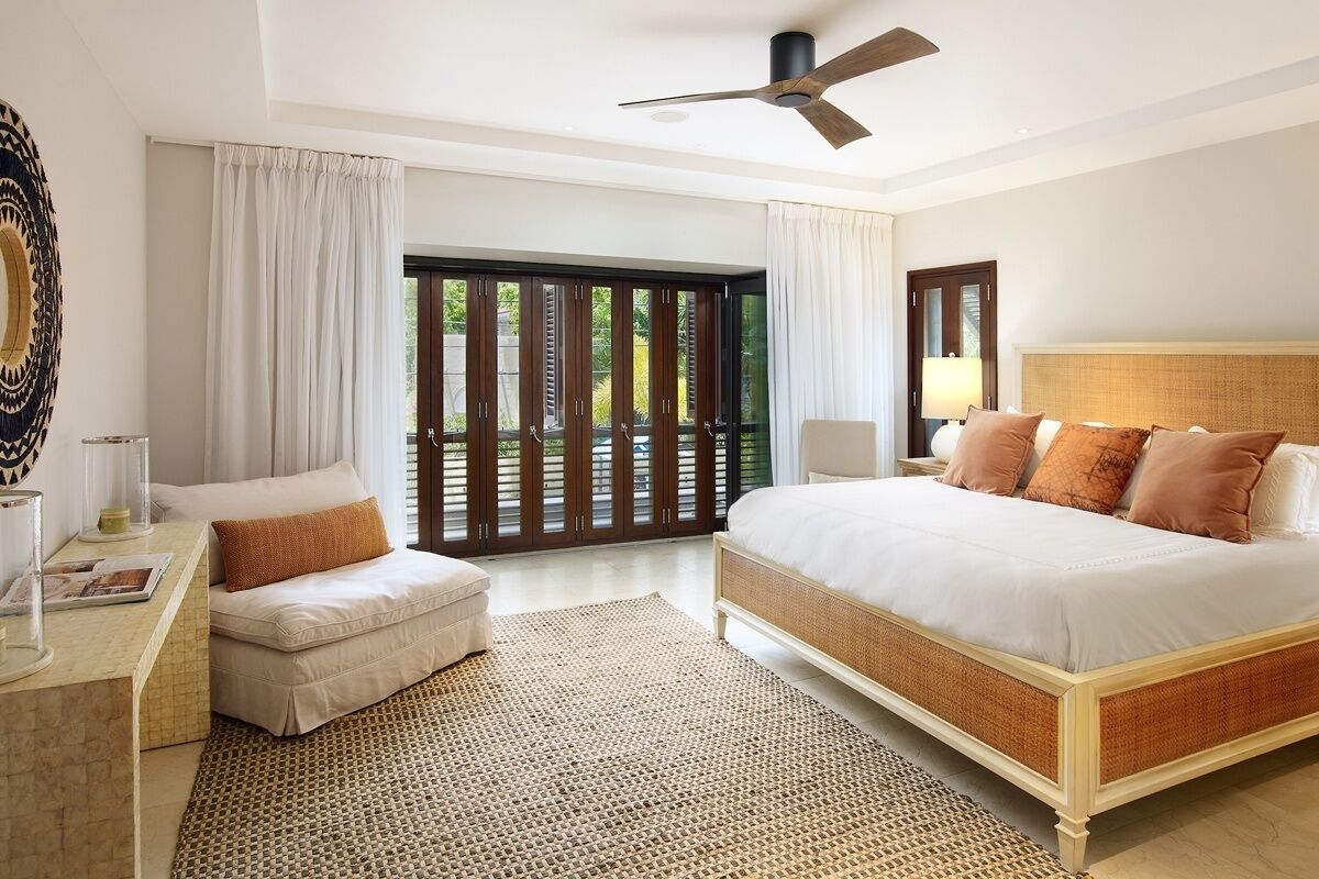 A bedroom with a large bed, a desk, a chair, a window with curtains, and a ceiling fan.