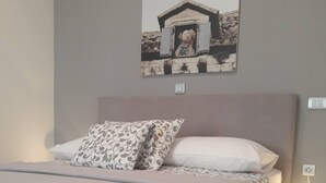 A neatly made bed with a patterned pillow and a white pillow, a bedside table with a lamp, and a wall-mounted picture. - Spacious studio apartment with a  terrace,parking,free WiFi and AC in Baška Voda (Baška Voda)