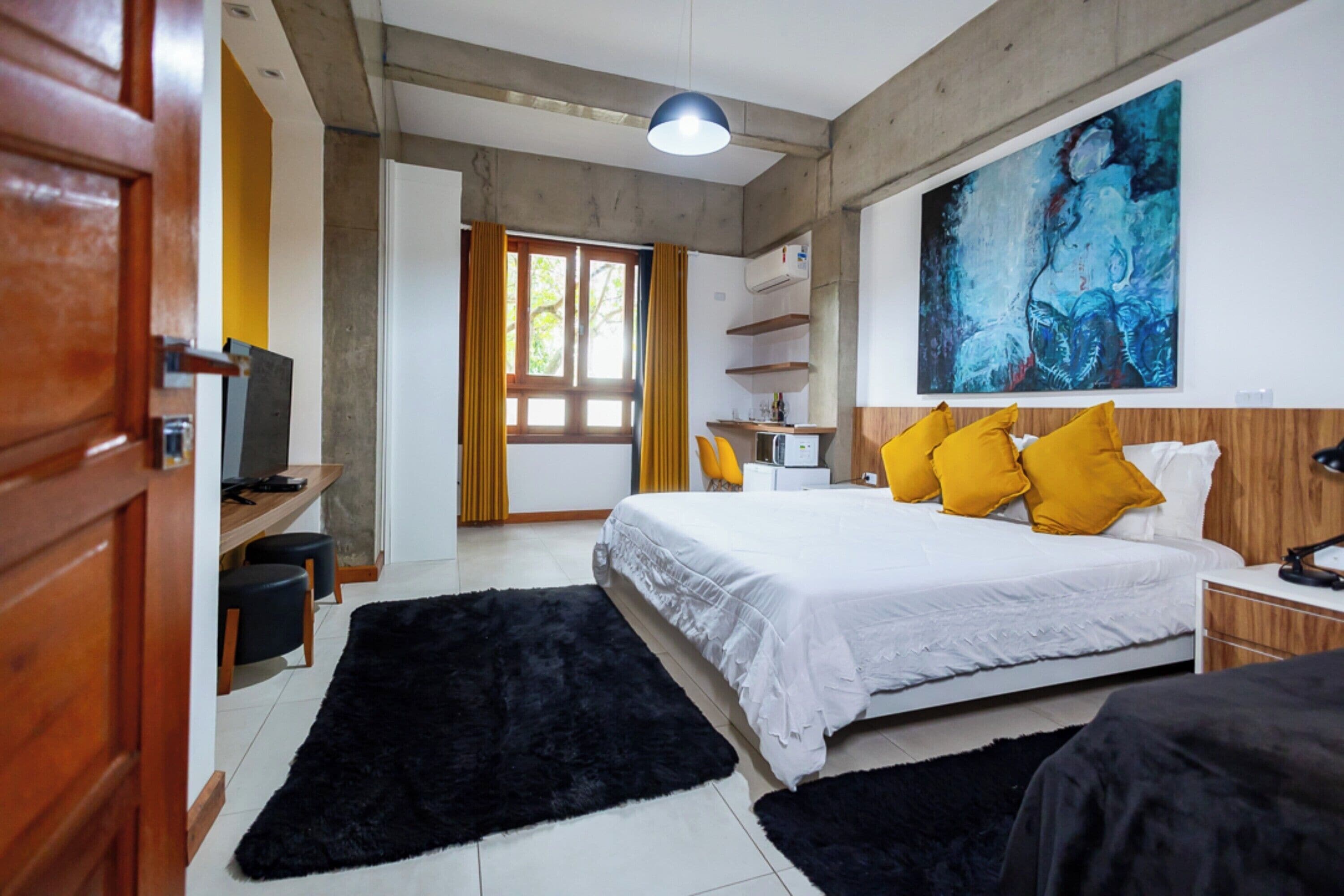 A modern hotel room with a large bed, a desk with a chair, a TV, and a large abstract painting on the wall.