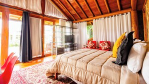 Un dormitorio amplio con una cama grande, techo de madera y un balcón con cortinas.