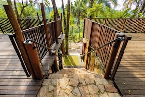 Una escalera de madera con barandillas de metal que lleva a una plataforma de piedra rodeada de abundante vegetación.