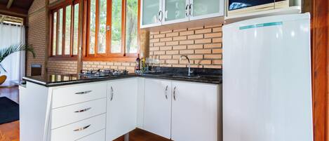A kitchen with white cabinets, a refrigerator, a microwave, and a window with a view of greenery.