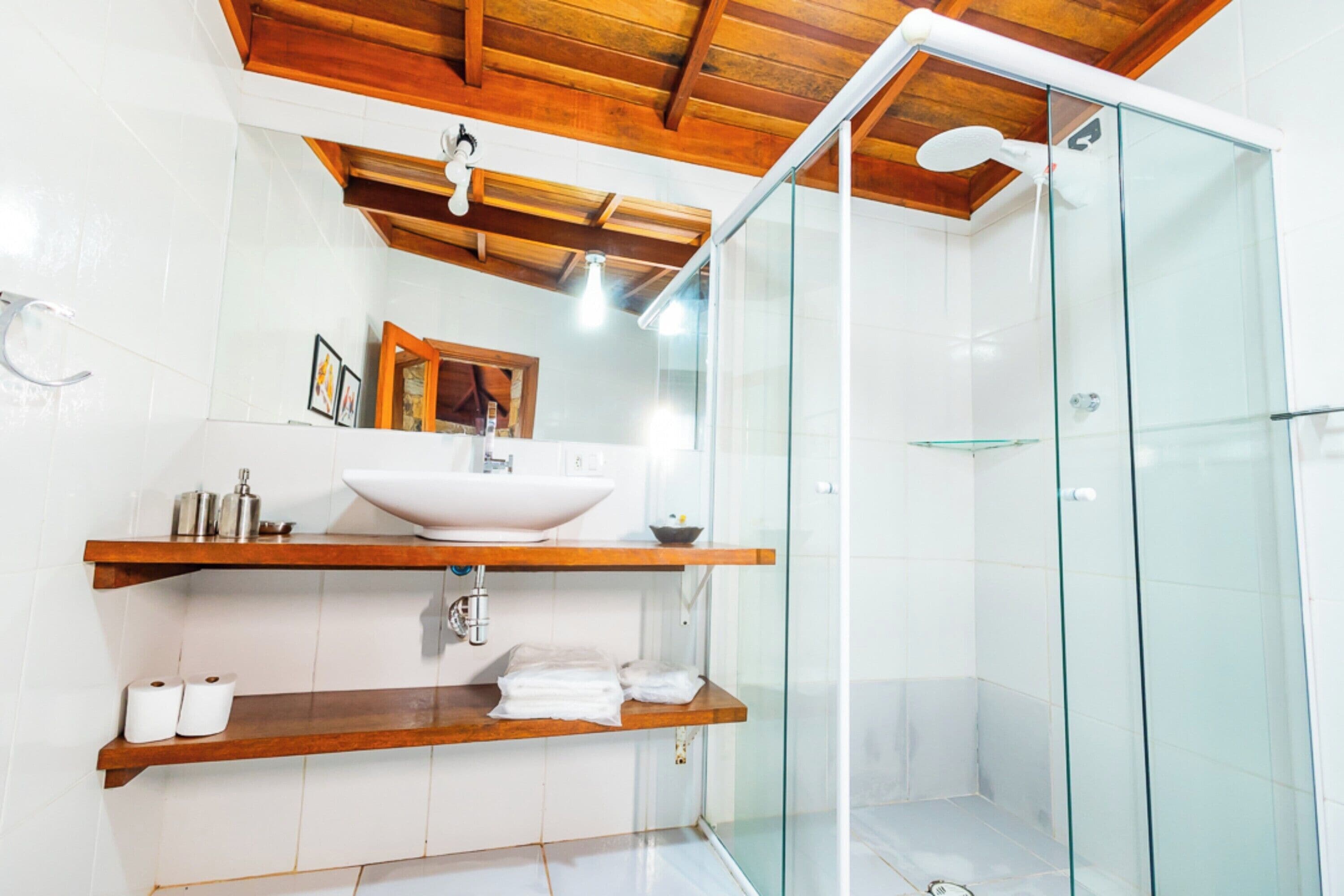 A modern bathroom with a glass-enclosed shower, a wooden ceiling, and white tiles.