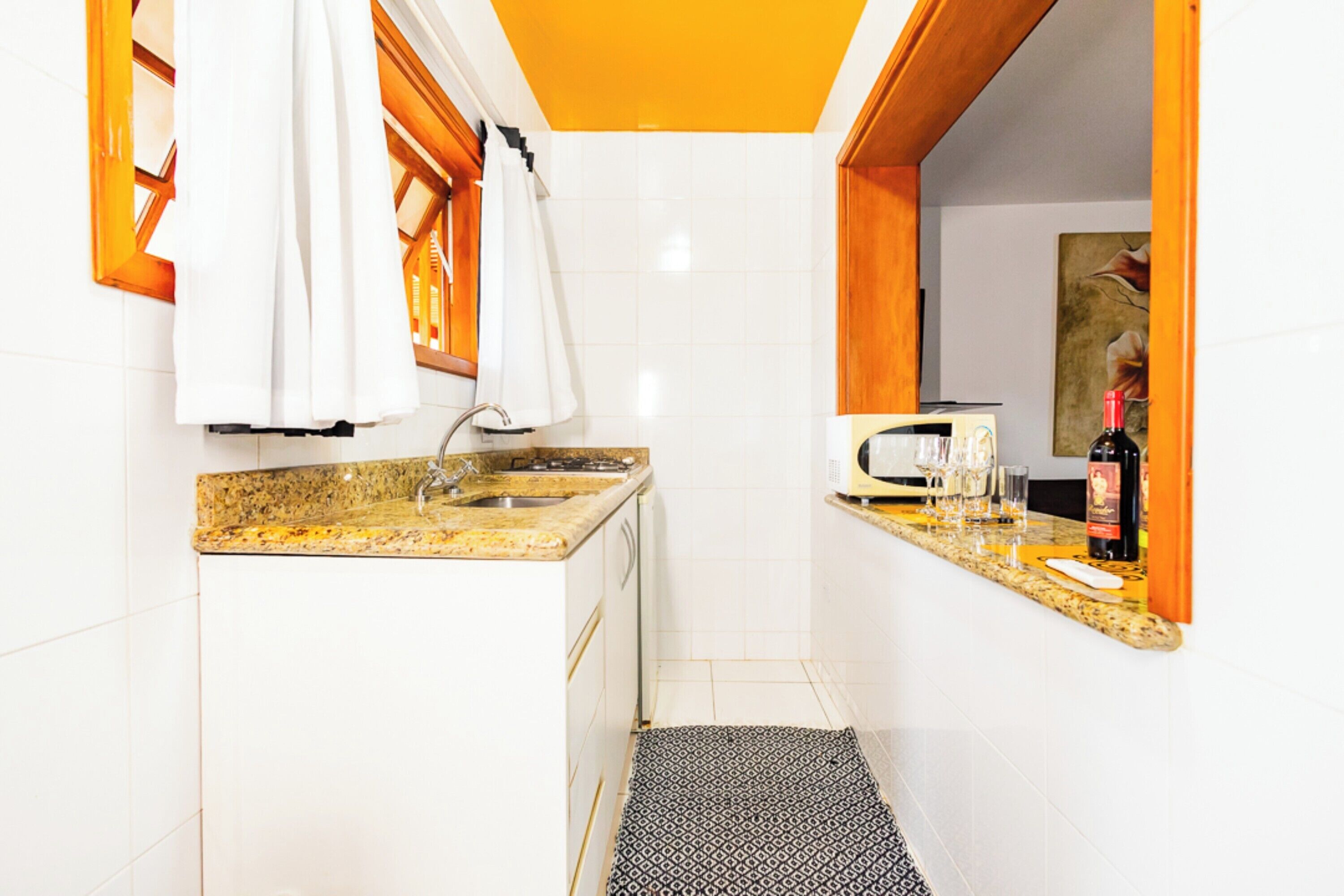 A compact kitchen with white cabinets, a granite countertop, a microwave, and a small sink.
