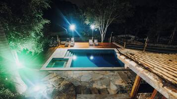 Una piscina con terraza de piedra, rodeada de árboles y una terraza de madera.