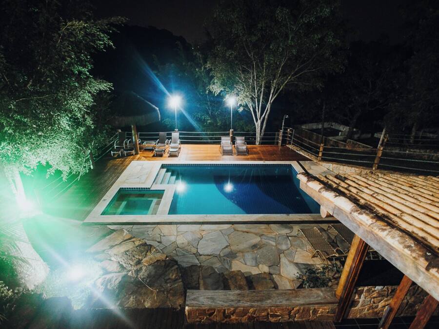 Una piscina con terraza de piedra, rodeada de árboles y una terraza de madera.