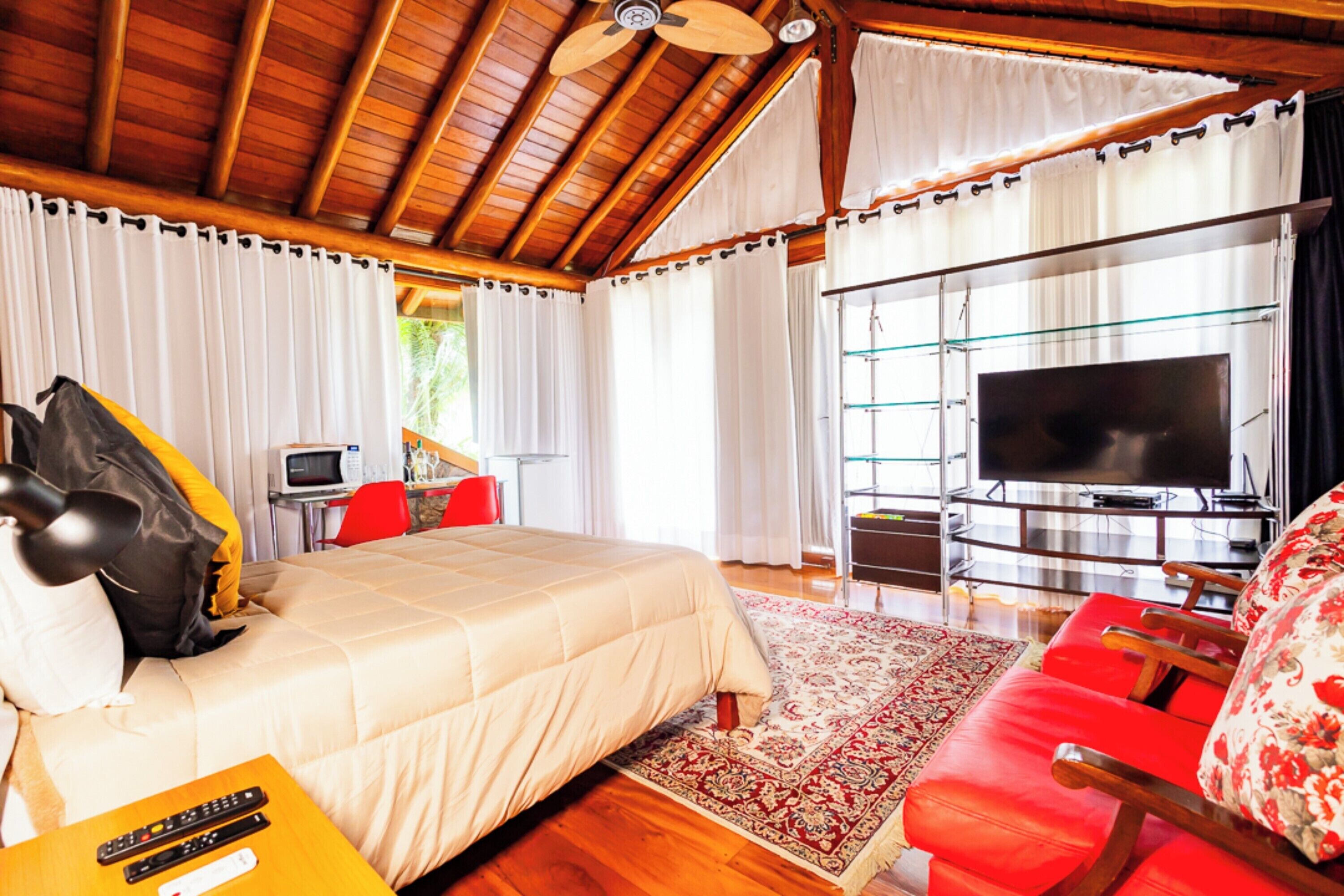 Um quarto espaçoso com uma cama grande, um sofá vermelho, uma televisão e teto de madeira.