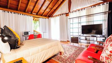 Um quarto espaçoso com uma cama grande, um sofá vermelho, uma televisão e teto de madeira.
