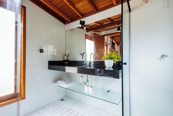 Un baño moderno con repisa de vidrio, encimera negra y una planta en maceta.