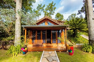 Una cabaña de madera con porche, rodeada de abundante vegetación y árboles.