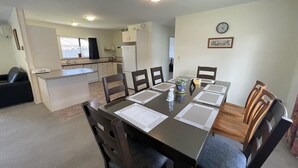A dining area with a table set for six, surrounded by wooden chairs. There is a kitchen in the background with white cabinets and a refrigerator. - Perfect for Large group-Near Redwood Forest (Rotorua)