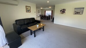 A living room with a black leather sofa, a wooden coffee table, and a dining area with a table and chairs. - Perfect for Large group-Near Redwood Forest (Rotorua)