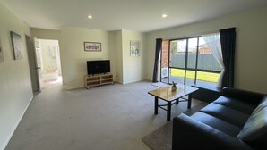 A living room with a TV, a sofa, a coffee table, and a sliding glass door leading to a backyard. - Perfect for Large group-Near Redwood Forest (Rotorua)
