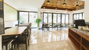 A modern cafe with wooden tables and chairs, a coffee machine, and large windows allowing natural light. - Thapae Twins Hotel (Chiang Mai)