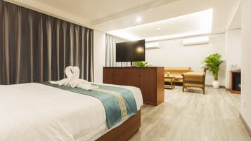 A hotel room with a bed, a desk, a chair, a television, and a potted plant.