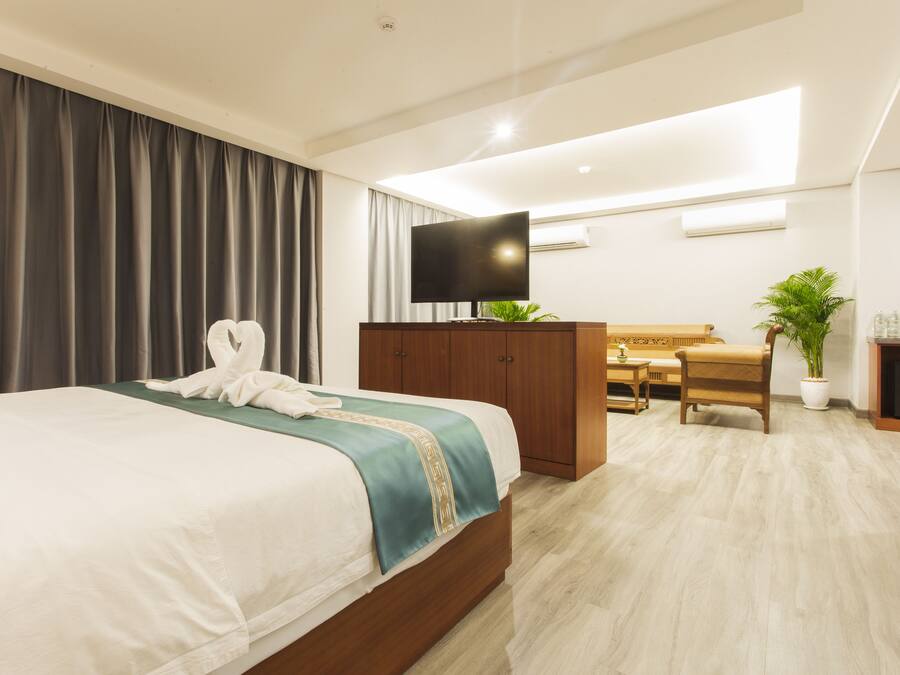 A hotel room with a bed, a desk, a chair, a television, and a potted plant.