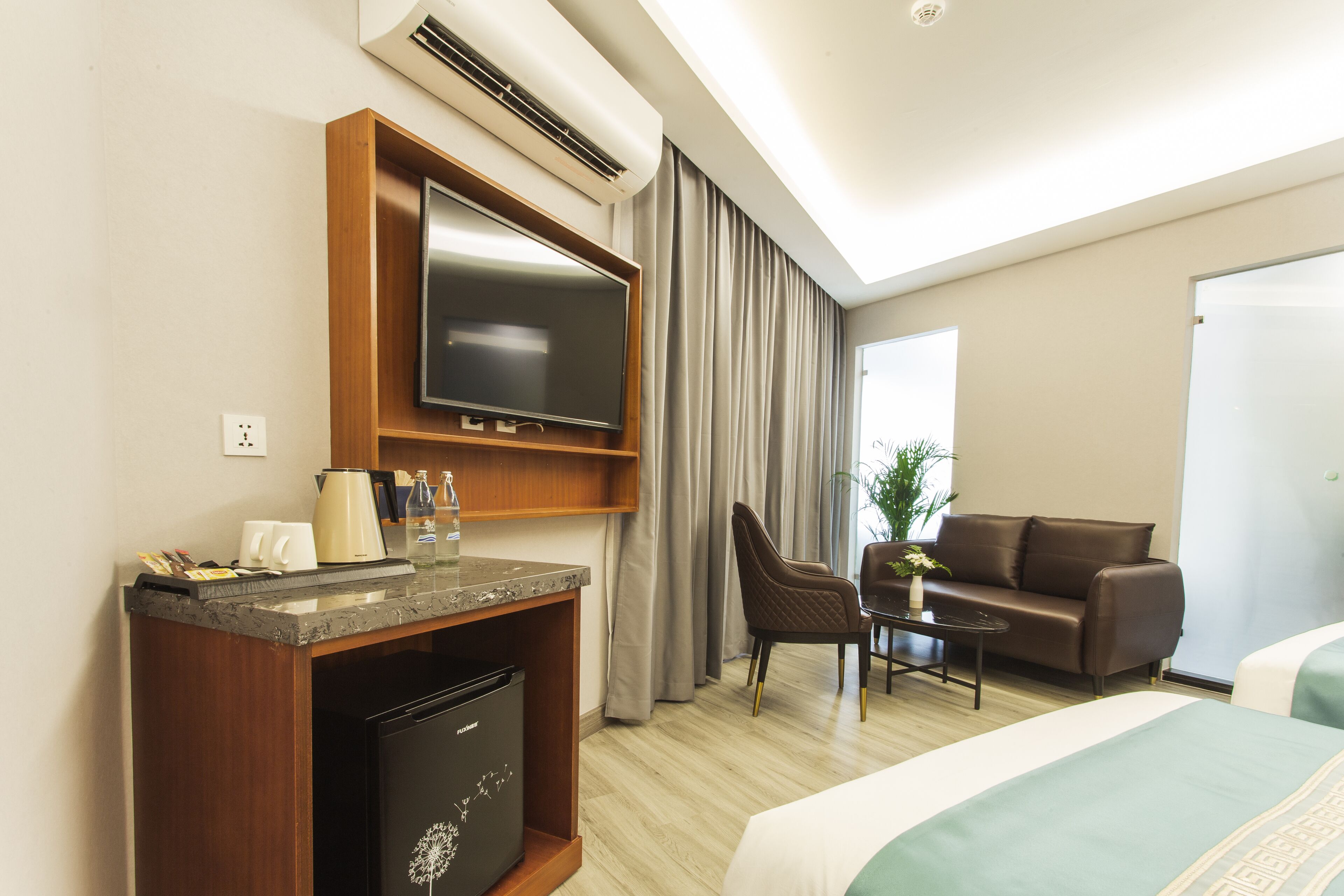 A hotel room with a bed, a desk with a television, a coffee maker, and a small refrigerator.