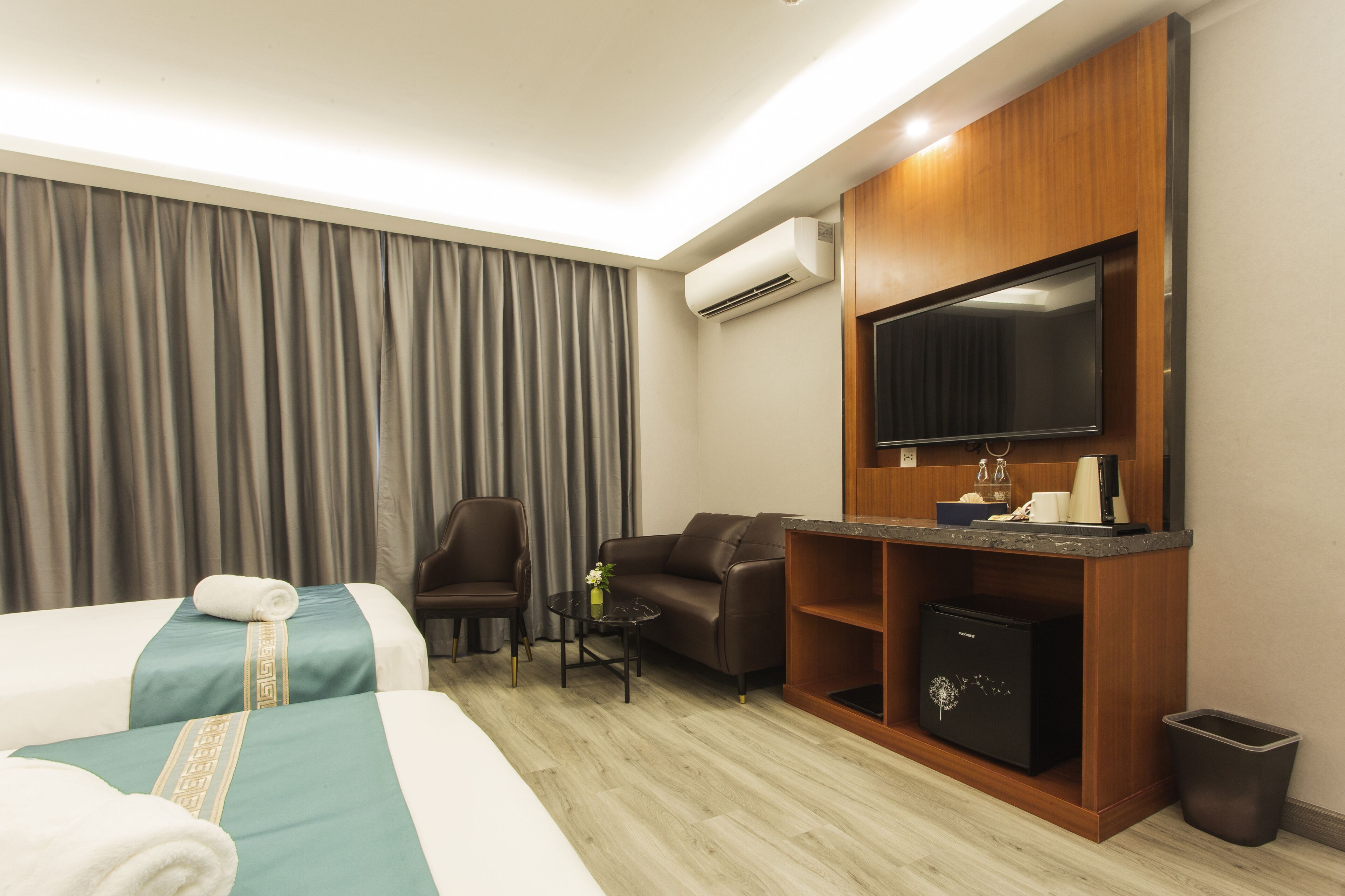 Quarto de hotel com duas camas, um sofá, uma mesa pequena, uma televisão e um minibar.