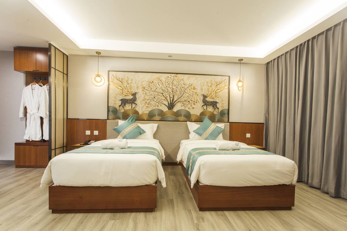 Ein Hotelzimmer mit zwei Betten, einem Kleiderschrank, einem Spiegel und einem an der Wand hängenden Kunstwerk.