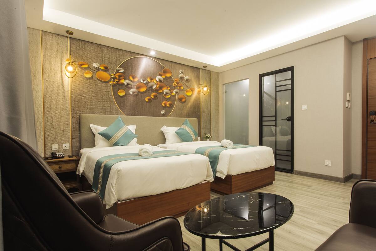 Ein Hotelzimmer mit zwei Betten, einer Sitzecke mit Tisch und einem dekorativen Wandbild.